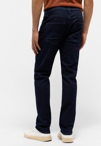 Granatowe dżinsy z prostym krojem, z dwiema tylnymi kieszeniami ozdobionymi przeszyciami oraz kontrastowym paskiem. Noszone z białymi sneakersami.