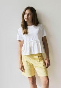 Vit kortärmad topp med en figursydd bodice och utfläkt peplum. Matchad med ljusgula linneshorts med sidfickor.