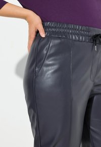 Mörkgrå läderbyxor med elastisk midja och dragsko, sidofickor och en slät yta.