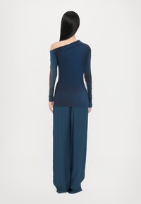 Schulterfreies Oberteil in Marineblau mit langen Ärmeln, kombiniert mit weit geschnittenen, fließenden Hosen. Glattes Material mit dezenten Farbverlauf-Details.