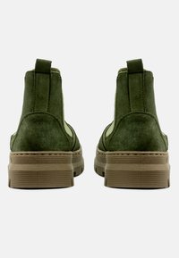 Stivaletti alla caviglia in suede verde con punta tonda, pannelli laterali elastici e suola texturizzata color talpa. Presentano un pratico anello sul retro per indossarli facilmente.