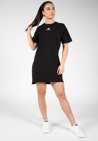 Zwarte katoenen t-shirt jurk met korte mouwen en een ronde hals. Heeft logo details op de borst en zijsplitten aan de zoom.