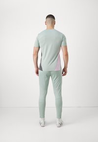 Sportoutfit in lichtgroen, met korte mouwen en strakke broek. Panelen in donkergrijs en lichtroze voegen contrast toe. Gladde textuur.