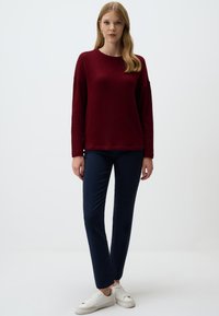 Bordeaux gebreide trui met een geribbelde textuur, lange mouwen en een ronde hals, gecombineerd met marineblauwe slim-fit broek en witte sneakers.