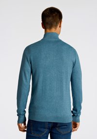 Herrtröja i teal-färg med hög krage och långa ärmar. Tillverkad i ett mjukt stickat tyg med ribbade detaljer vid ärmsluten och nederkant.