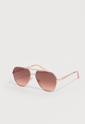 Rózsaszín pilótaszemüveg barna átmenetes lencsékkel. Fém keret, melynek szára láncszemes díszítéssel rendelkezik. Simára csiszolt, tükröződő felület.