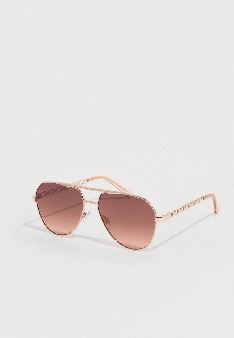 Ροζ γυαλιά ηλίου πιλότου με σταδιακού χρώματος καφέ φακούς. Μεταλλικό πλαίσιο με διακοσμητική αλυσίδα στα πλαϊνά. Λείο, αντανακλαστικό φινίρισμα.