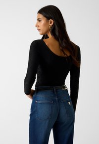 Czarny body z długim rękawem i wycięciem na plecach, połączony z ciemnoniebieskimi jeansami z wysokim stanem i trójkątnym logo na tylniej kieszeni.