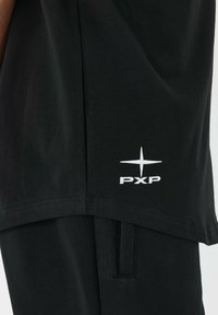 Camiseta de algodón negra con el logotipo blanco "PXP" y diseño de estrella en el bajo. Textura suave con un ajuste regular y sin patrones.
