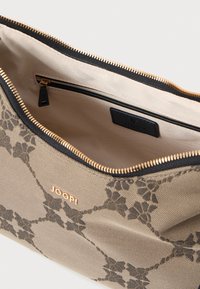 Beige JOOP! pung med mørkt blomster mønster, guldbelægning, sort lynlås og glat indre foring. Har en lille slip-lomme og logo-tag.