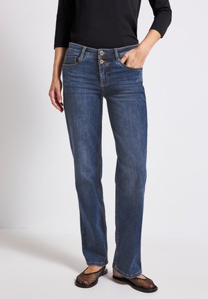 Blue denim jeans with a straight cut, featuring a button fly, five-pocket design, and visible stitching details. Worn with black mesh shoes.
