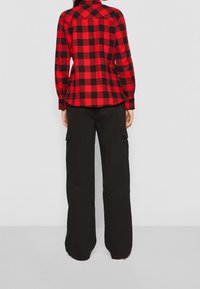 Chemise en flanelle à carreaux rouges et noirs, manches longues, poignets à boutons et design avec empiècement au dos, associée à un pantalon cargo noir ample.