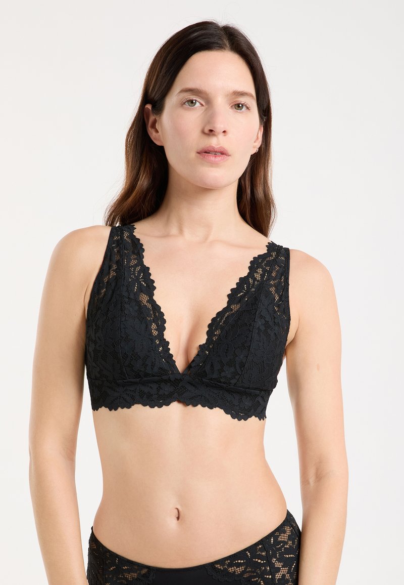 Schwarzes Spitzen-Bralette mit tiefem V-Ausschnitt, geschwungenen Kanten und breiten Trägern. Weiche Textur mit floralen Musterdetails.