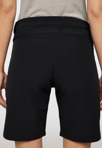 Mustat shortsit, joissa on sileä rakenne, leveä vyötärönauha ja suora leikkaus. Ei näkyviä kuvioita. Helma on hienovaraisesti käännetty.