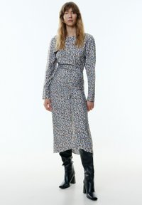 Bloemenprint lange mouw jurk met een getailleerde taille, knielange rok en een mix van blauwe, gele en roze patronen. Gecombineerd met zwarte laarzen tot de knie.