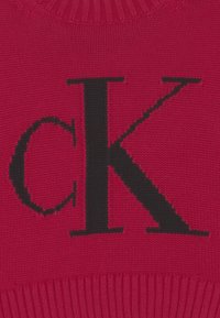 Červený pletený svetr s výrazným černým logem "CK". Textura je hladká, s vroubkovaným výstřihem a lemem.