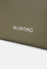 Olīvu zaļš teksturēts ādas virsma ar sudraba metāla burtiem, kas veido vārdu "VALENTINO", centrā tuvu apakšējai malai.