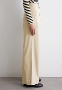 Beige hoge taille wijde broek met zijzakken en een gladde textuur, gecombineerd met een zwart-wit gestreepte longsleeve.