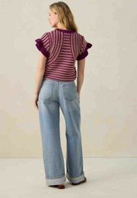 Haut tricoté violet à manches courtes avec des rayures multicolores, associé à un jean large bleu clair, avec des poignets retroussés et des poches arrière.