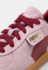 Rosa Wildleder-Sneaker mit roten Schnürsenkeln und Akzenten, ausgestattet mit einem goldenen Logo-Tag und einer strukturierten Gummisohle.
