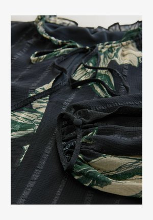 Čierne šaty z textúrovanej látky so zelenými a krémovými kvetinovými vzormi. Detaily zahŕňajú šnúrky na stiahnutie a nariasené rukávy.