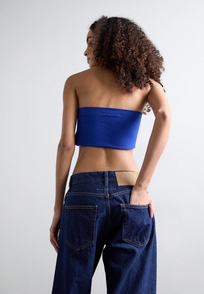 Modrý bandeau top skombinovaný s voľnými tmavými džínsami, ktoré majú zadné vrecká a textúrovaný pásový akcent blízko zadnej časti.