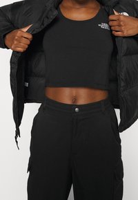 Chaqueta de plumas negra desabrochada, revelando un top corto negro ajustado y pantalones negros a juego. El conjunto tiene una textura suave y un diseño minimalista.