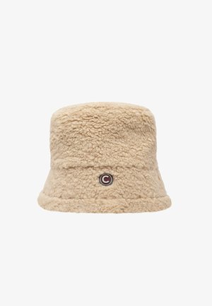 Bež bucket müts, mis on valmistatud pehmest, tekstuuriga materjalist. Sellel on külgedel ümmargune logo silt ja lai, paindlik ääre.