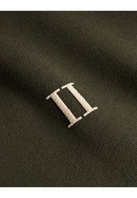 Mørkegrønt stof med en blød tekstur har et broderet hvidt "II" i en enkel serif skrift.