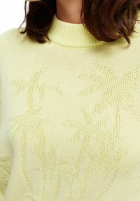 Suéter de color amarillo claro de punto con un cuello alto, que presenta patrones de palmeras texturizados. Material suave y liviano con acentos de canalé.
