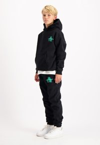 Zwarte hoodie en broek van een katoenmengsel, met groene grafische ontwerpen. Gecombineerd met een wit T-shirt en witte sneakers.