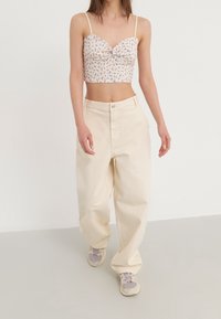 Top court floral avec un centre noué, associé à un pantalon beige clair à coupe décontractée et des baskets gris-violet. Design simple et texture douce.