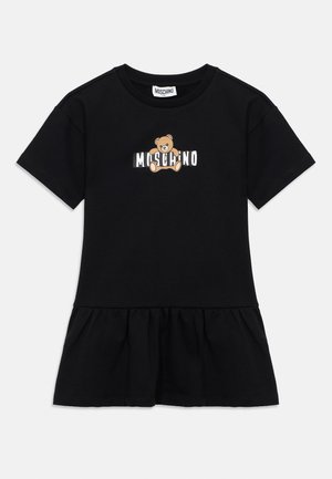 Rochie neagră cu mâneci scurte, din bumbac, având o fustă evazată. Partea frontală are un desen cu urs și textul „Moschino” în alb și maro.