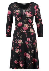 Robe noire longueur genoux avec motif floral rose et crème, encolure en V avec incrustation en dentelle et manches trois-quarts.