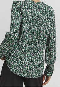 Blusa floreale verde con piccoli motivi bianchi, rosa e viola chiaro, dettaglio plissettato sul retro e maniche lunghe con polsini aderenti.