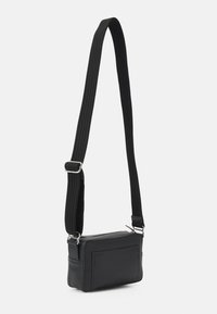 Petit sac bandoulière rectangulaire noir avec une sangle ribbed ajustable et quincaillerie argentée sur fond blanc uni.