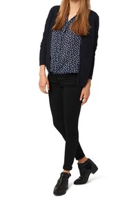 Black skinny jeans, navy knit cardigan, and patterned blouse featuring white flowers on a dark background. Black ankle boots with bow detail.
