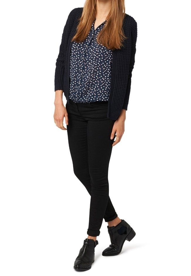 Black skinny jeans, navy knit cardigan, and patterned blouse featuring white flowers on a dark background. Black ankle boots with bow detail.