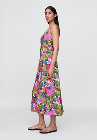 Vestido maxi floral com padrões vibrantes em rosa, azul e verde, alças finas e corte solto. O tecido parece leve e suave.