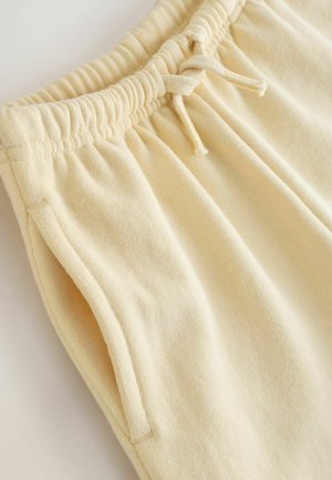 Sárga pamut melegítőnadrág, elasztikus derékkal, húzózsinórral és oldalsó zsebekkel. Az anyag puha, texturált felületű.