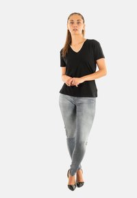 T-shirt nera con scollo a V e maniche corte, abbinata a jeans skinny grigi chiari e scarpe con tacco nere. Design semplice e aderente.