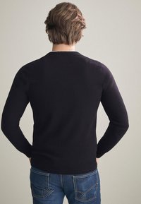 Svart stickad tröja med långa ärmar och rund halsringning, bärs med blå denimjeans som har två bakfickor. Strukturerad yta.