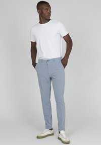 Pantalones ajustados de color azul claro con una textura suave, bolsillos frontales y cierre de un solo botón, combinados con una camiseta blanca sencilla y zapatillas.