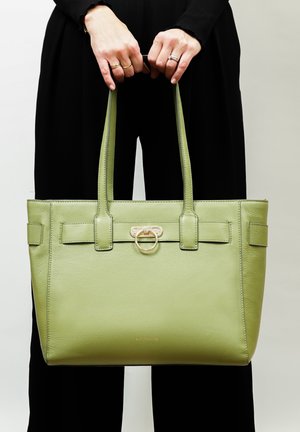Grüne Leder-Tote-Tasche mit doppelten Griffen, ausgestattet mit einem Ring aus goldfarbenem Metall und strukturiertem Design, präsentiert vor einem hellen Hintergrund.