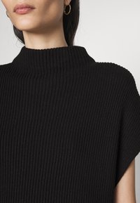 Schwarzer, gerippter Pullover mit hohem Kragen und strukturiertem Finish sowie kurzen Ärmeln, der ein tailliertes und strukturiertes Design aufweist.