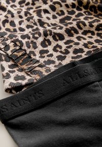 Leopardenmusterstoff mit gerippter Struktur, kombiniert mit schwarzen Leggings, die einen strukturierten Taillenbund mit dem Aufdruck "ALLSAINTS" haben.