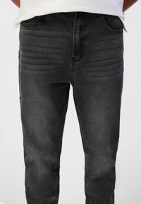 Jeans en denim noir à coupe slim, avec un léger délavage, quatre poches et une texture lisse. Coutures visibles le long des coutures.