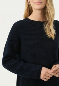 Sötétkék bordás kötött pulóver kerek nyakkal, hosszú ujjakkal és laza fazonnal. Az anyag részletein textúrált kivitel látható.