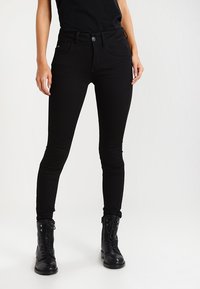 Los pantalones vaqueros skinny negros presentan una cintura alta, un diseño de cinco bolsillos y un cierre de botón, combinados con botas negras de cordones.