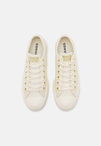 Beige bőr sportcipők fehér gumi orrborítással, arany fűzőlyukakkal és 'Converse All Star' felirattal a nyelvén. Lapos fűzők.